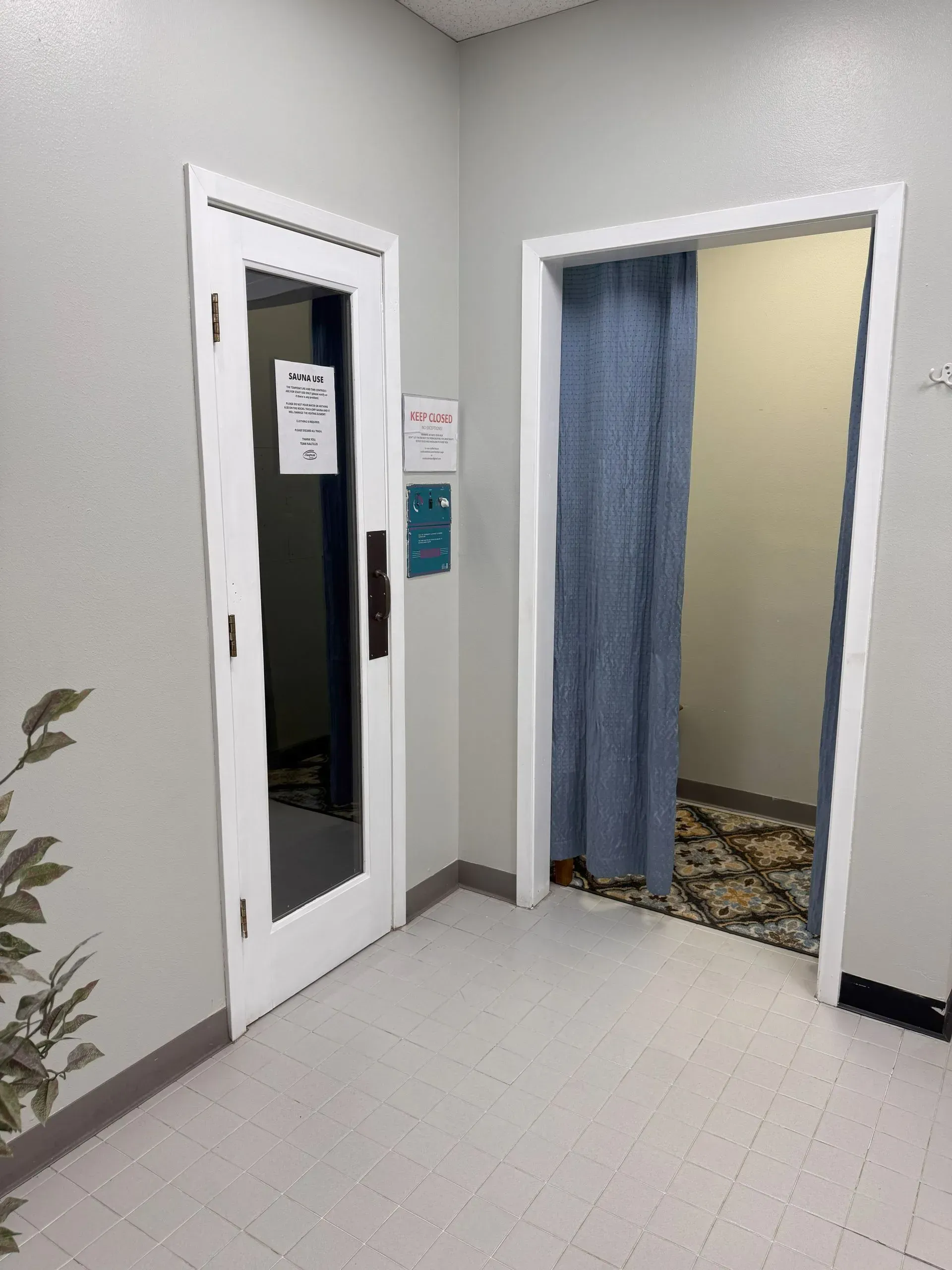 Two doorways in a corner of a room, one with a glass door, the other with a blue curtain.