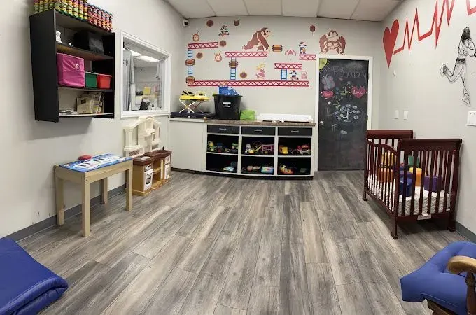 Daycare room with wooden floors, crib, tables, shelves, and colorful wall decorations.
