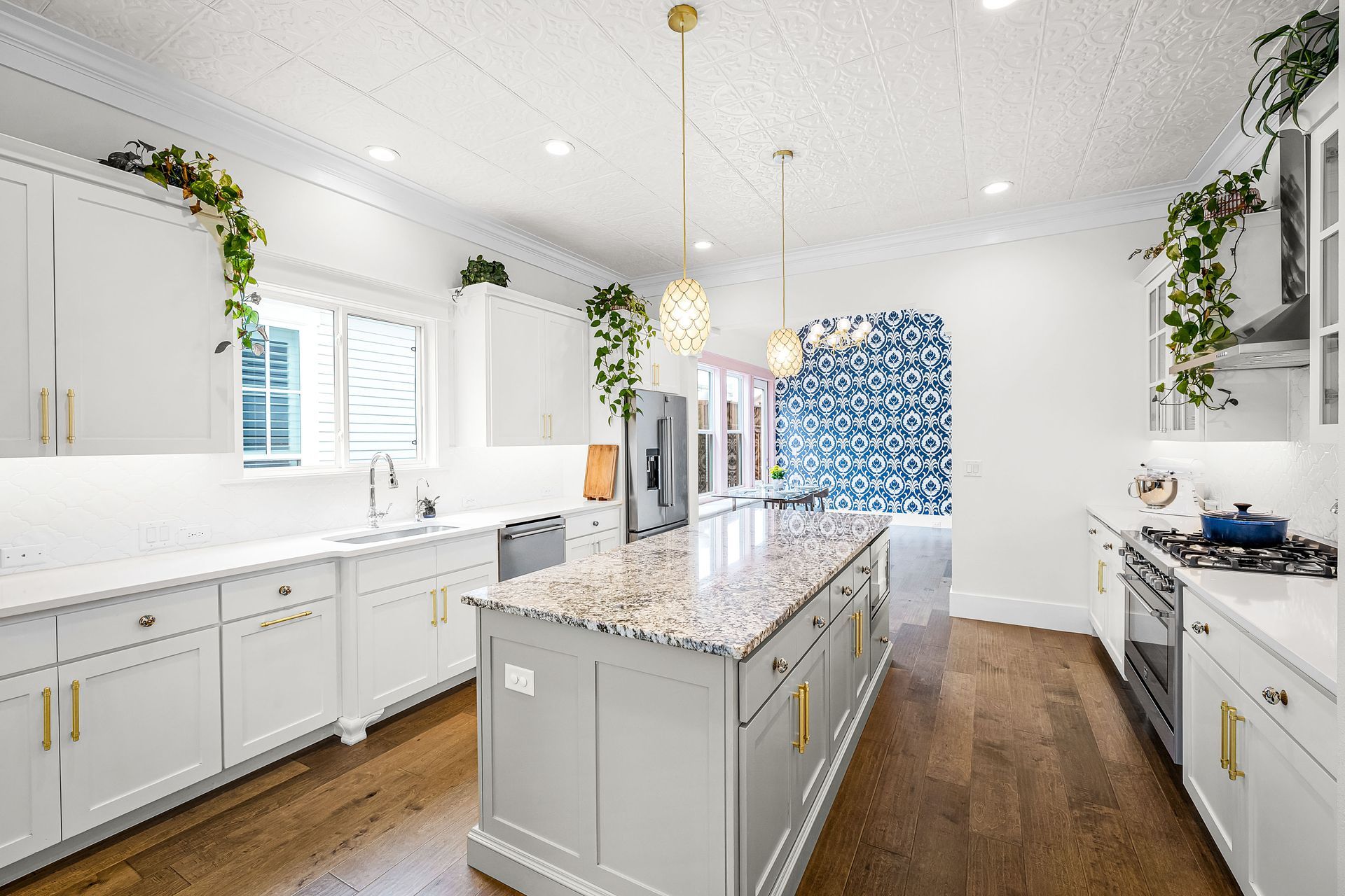 Bright white kitchen with marble island, gold pendant lights, and blue patterned curtains