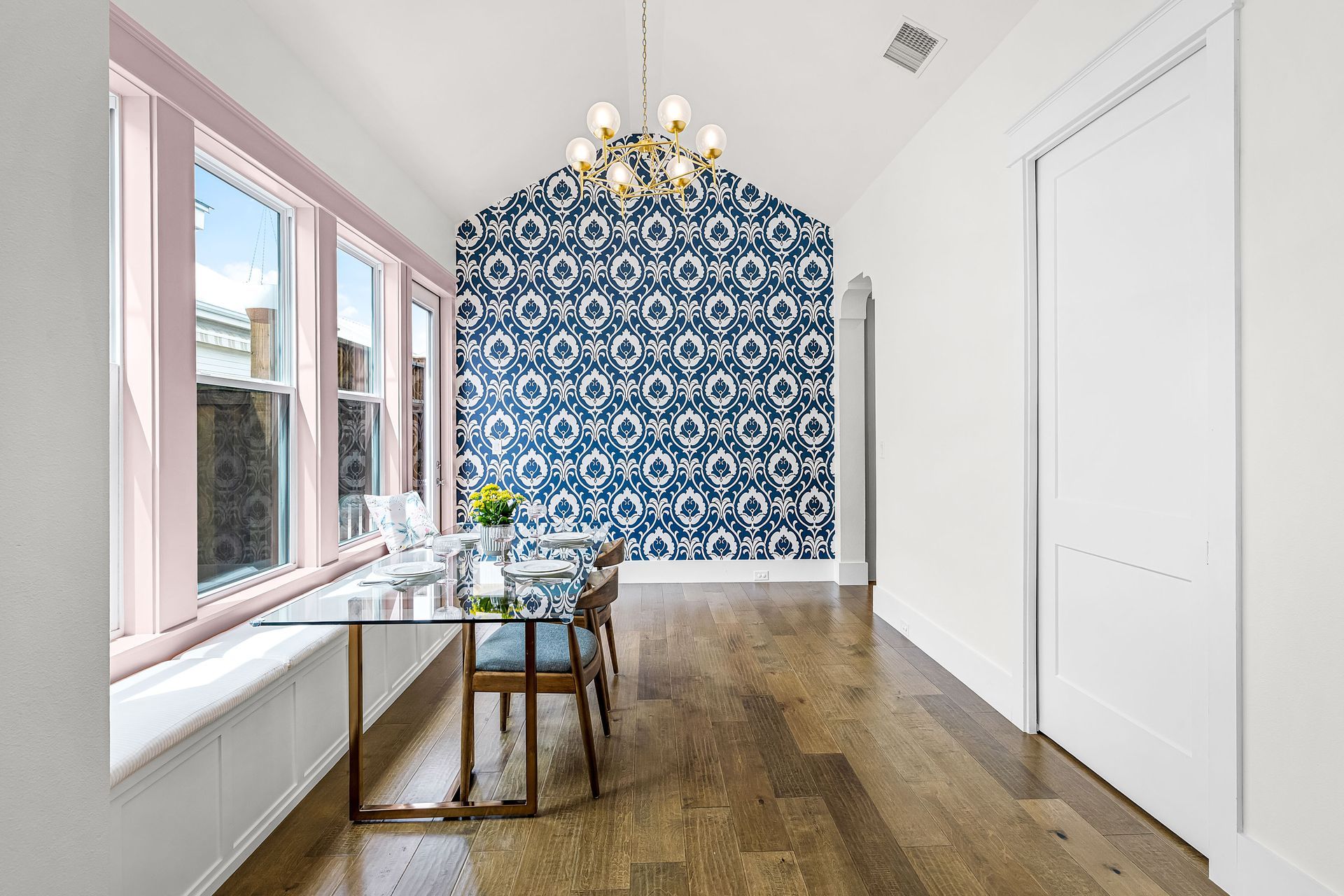 Bright dining room with blue patterned accent wall, chandelier, wooden table, and large windows