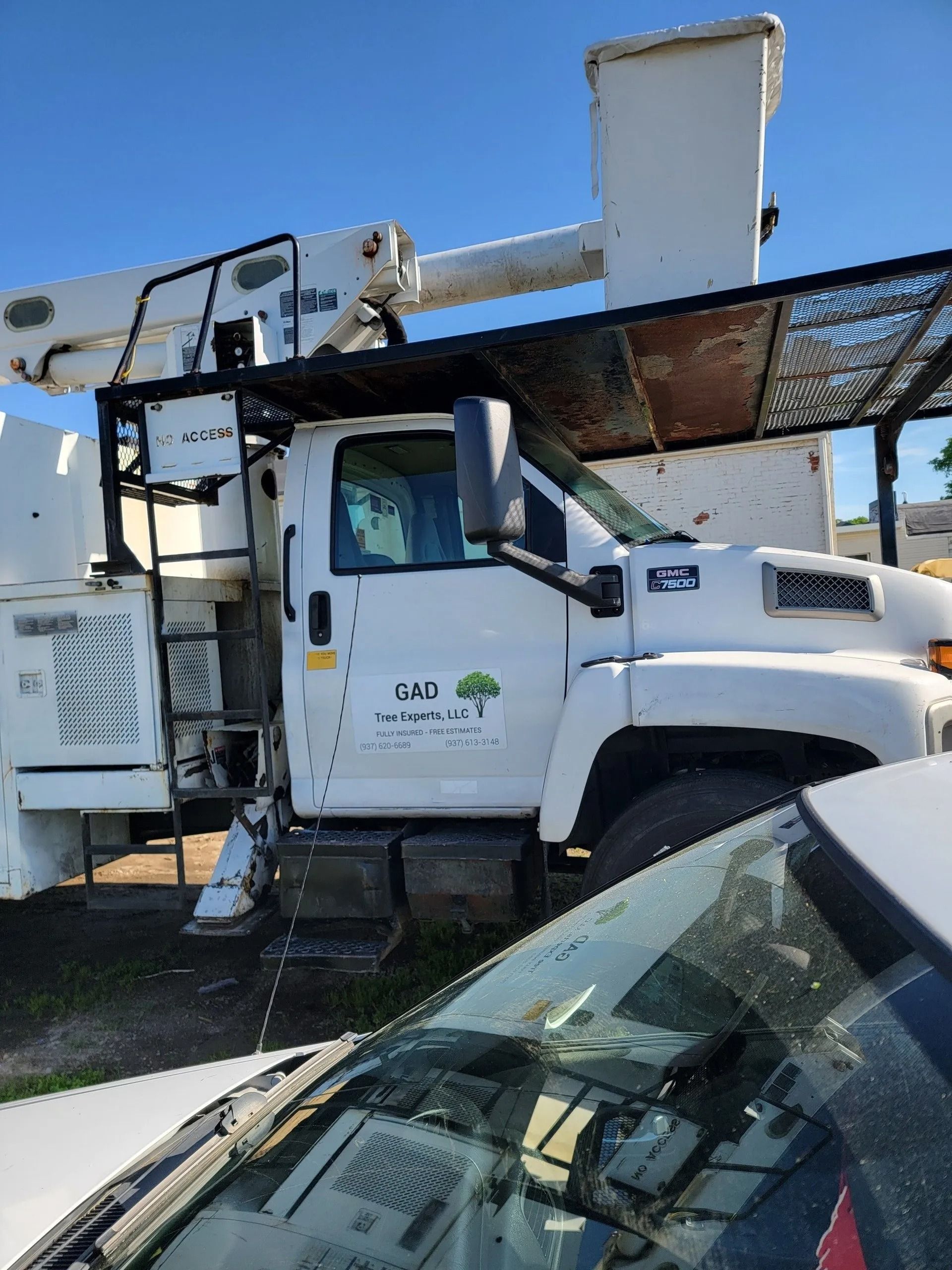 White tree service truck with an elevated bucket, parked outside.