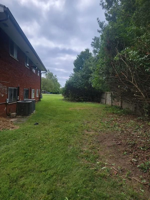 A grassy area next to a brick building and a line of trees under a cloudy sky.