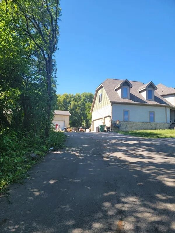 Asphalt driveway leading to a house with a light-colored exterior and a garage, under a bright blue sky.