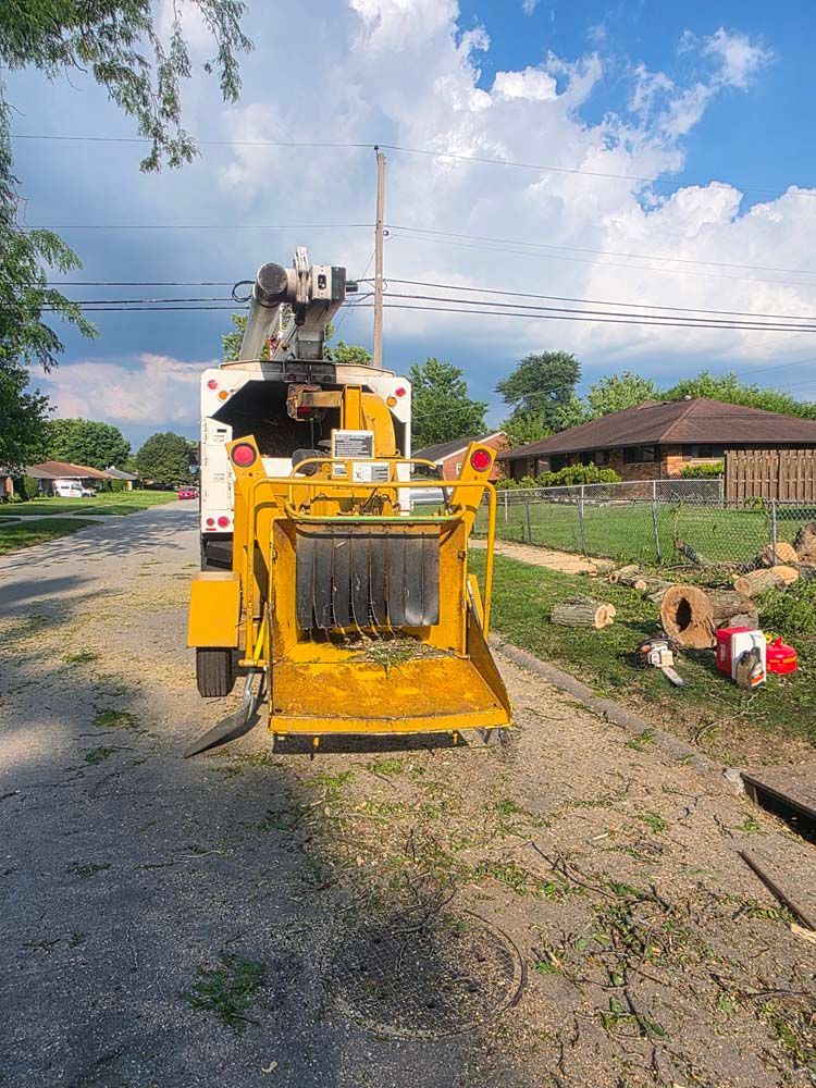 Yellow wood chipper on a gravel road, near a residential area.