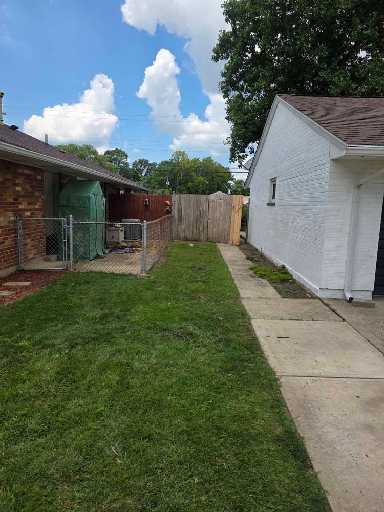 A backyard with green grass, a chain-link fence, and a wooden fence. A white brick garage is on the right.