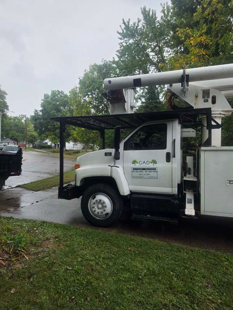 White tree service truck with extended arm parked on a wet street.