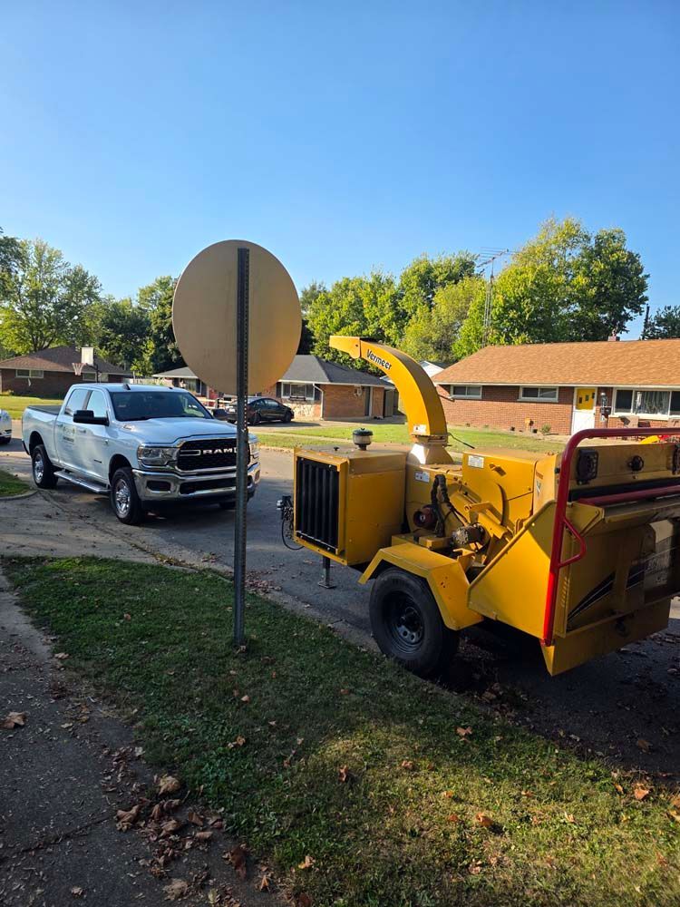White truck parked near a yellow wood chipper on a suburban street.