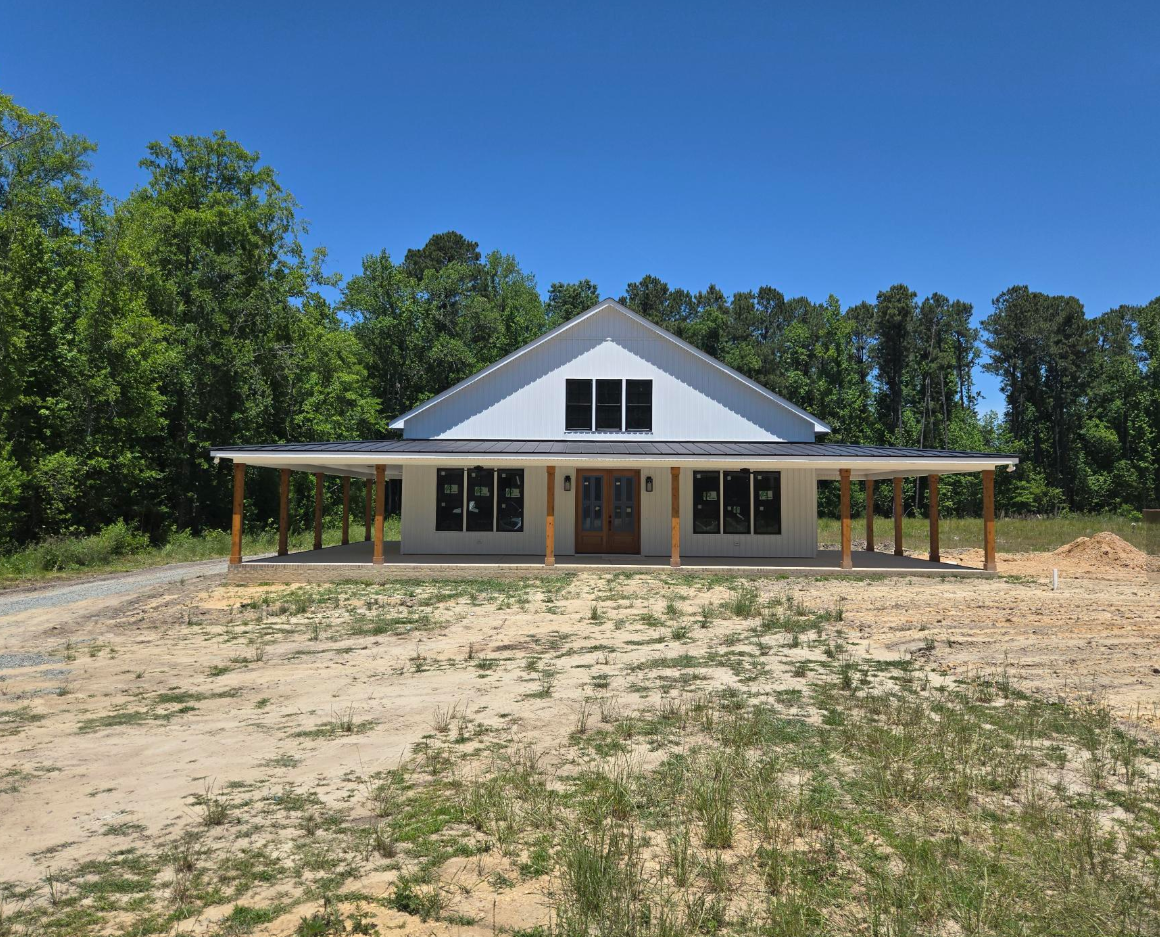 New white house with a front porch on a cleared lot under a bright blue sky