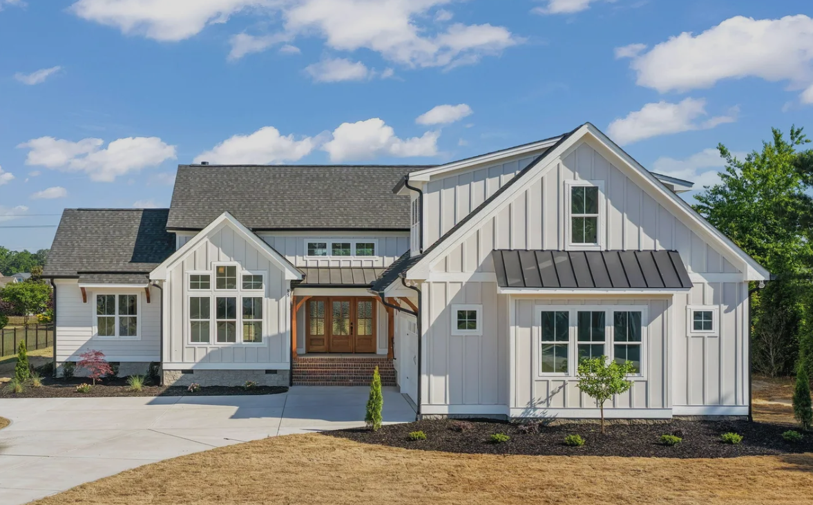 Modern white farmhouse-style house with gray roof, large windows, and a landscaped front yard