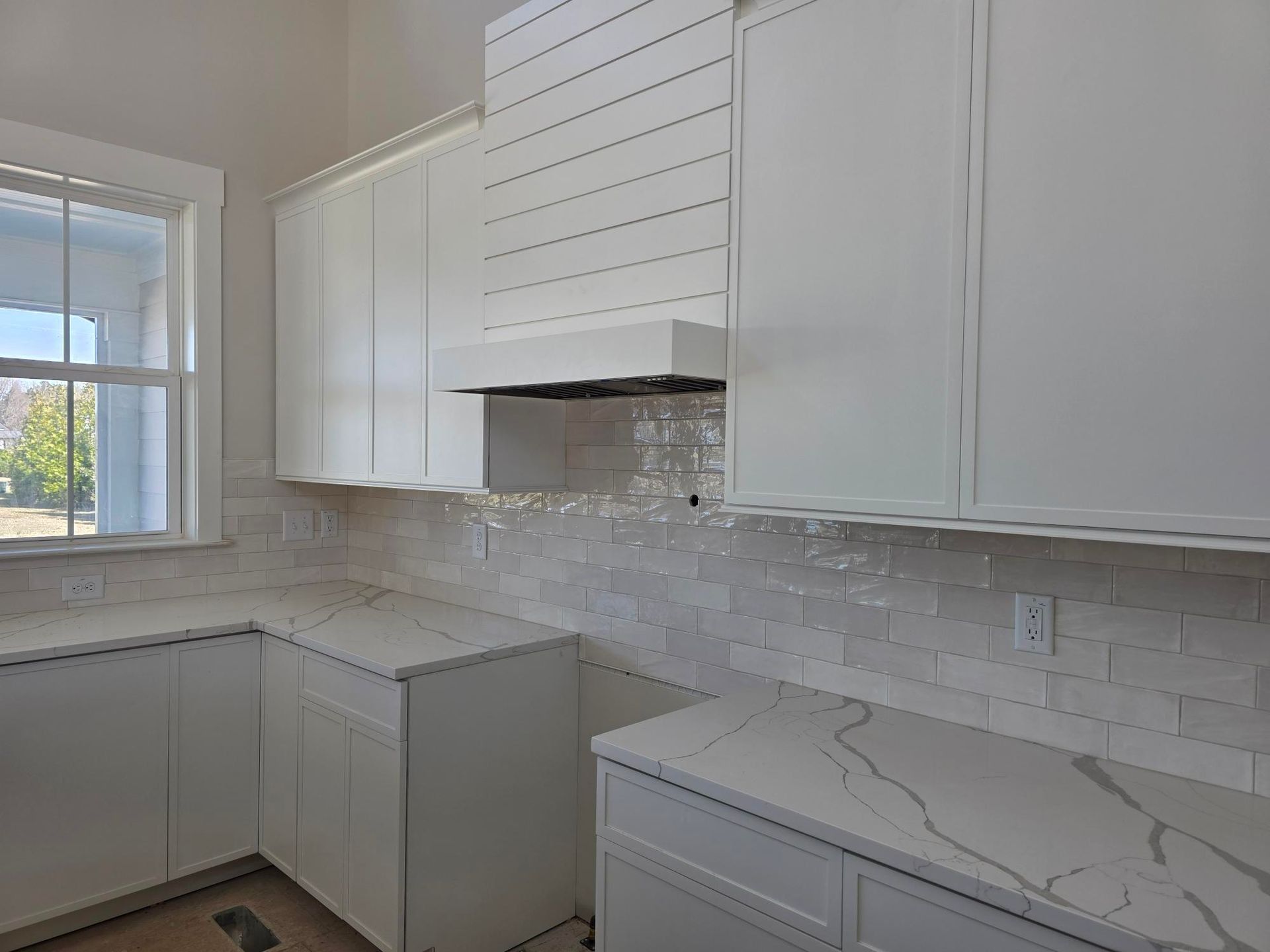 Bright white kitchen with marble-look counters, subway tile backsplash, and a window over the sink.