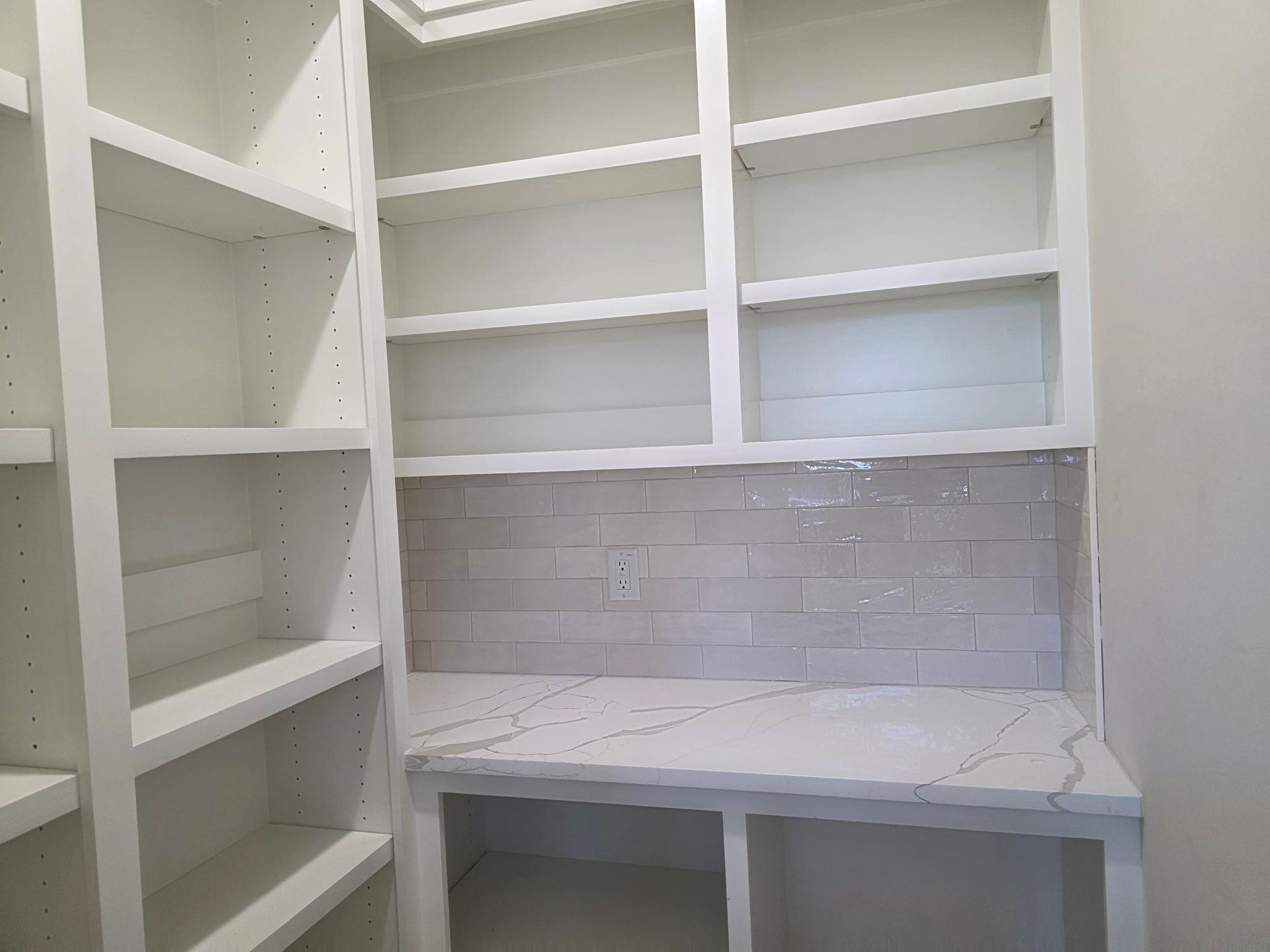 White built-in pantry with open shelves, marble-look countertop, and white subway tile backsplash.