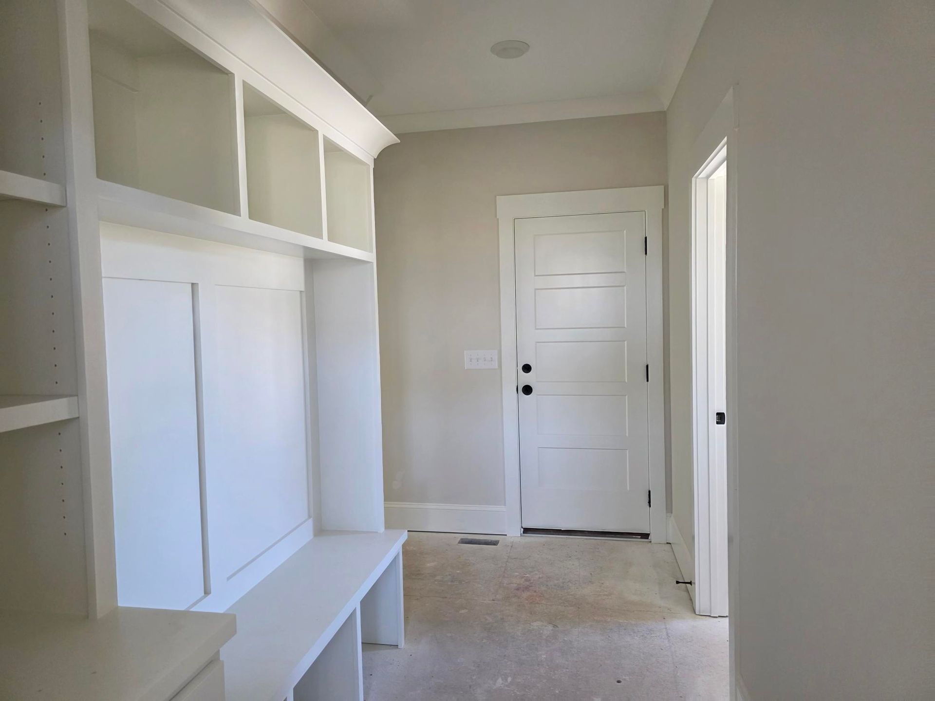 Empty white hallway with built-in shelves, a bench, and a closed door at the end.