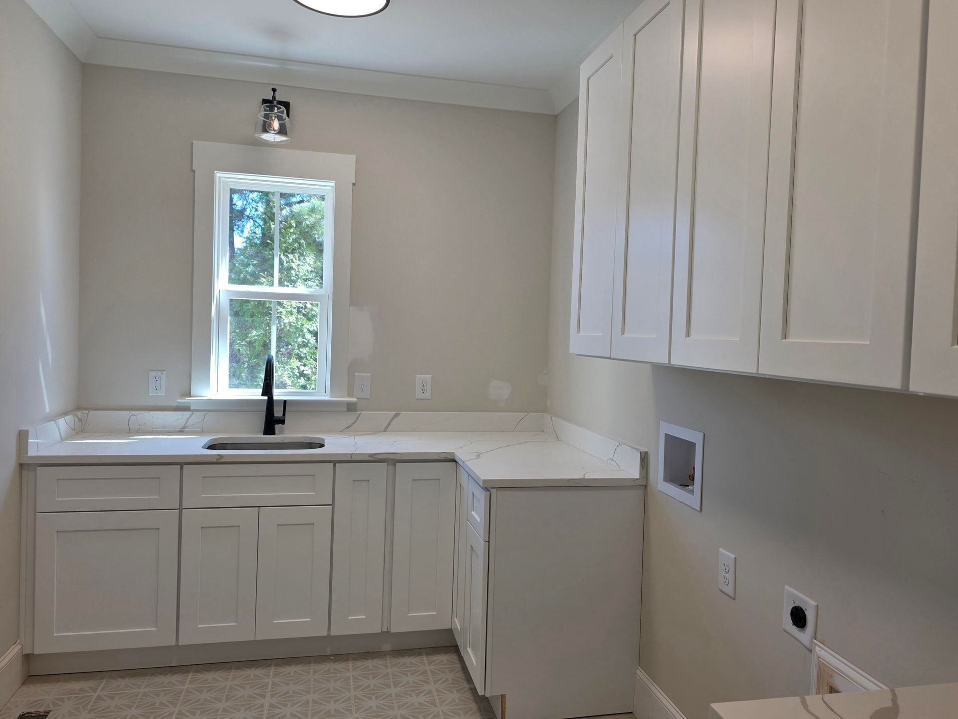 Bright white kitchen with cabinets, sink under window, and light countertops