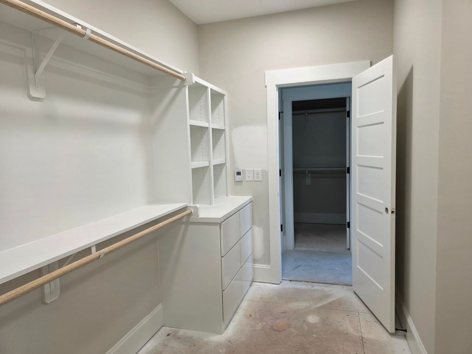 Walk-in closet with white shelves, hanging rods, and an open door to a small adjacent room