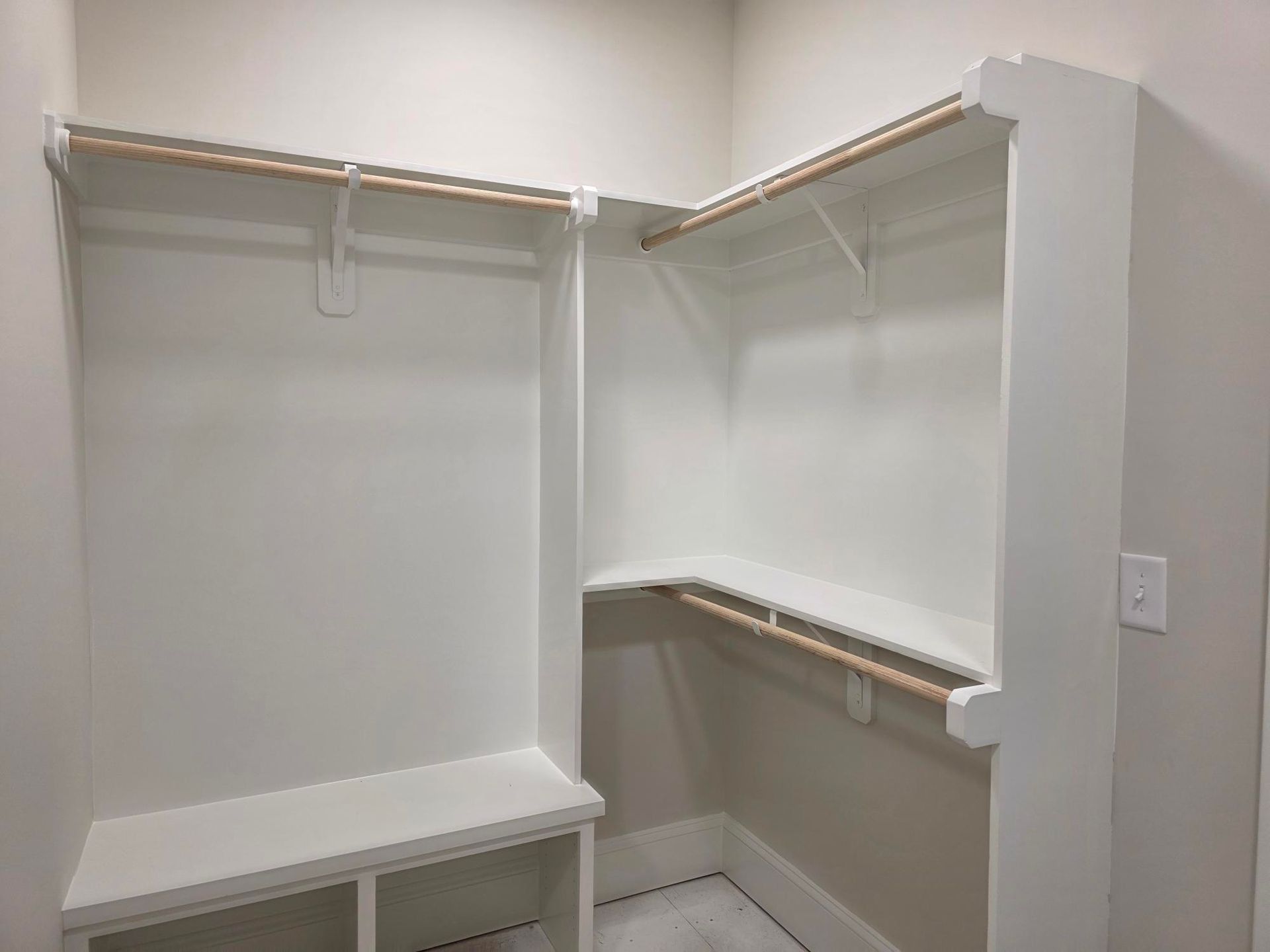 Empty white walk-in closet with shelves, hanging rods, and a bench in a corner alcove