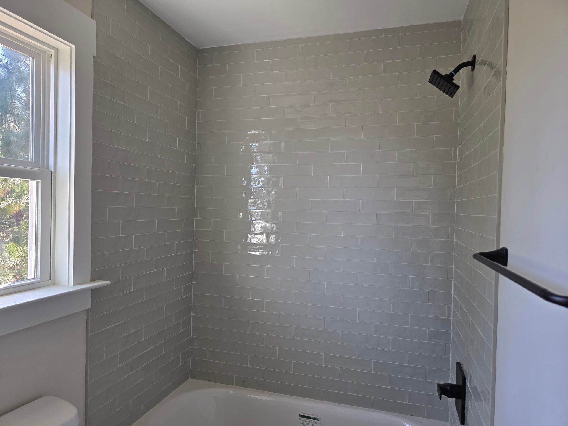 Small tiled bathroom shower with gray subway tile, black fixtures, and a window on the left