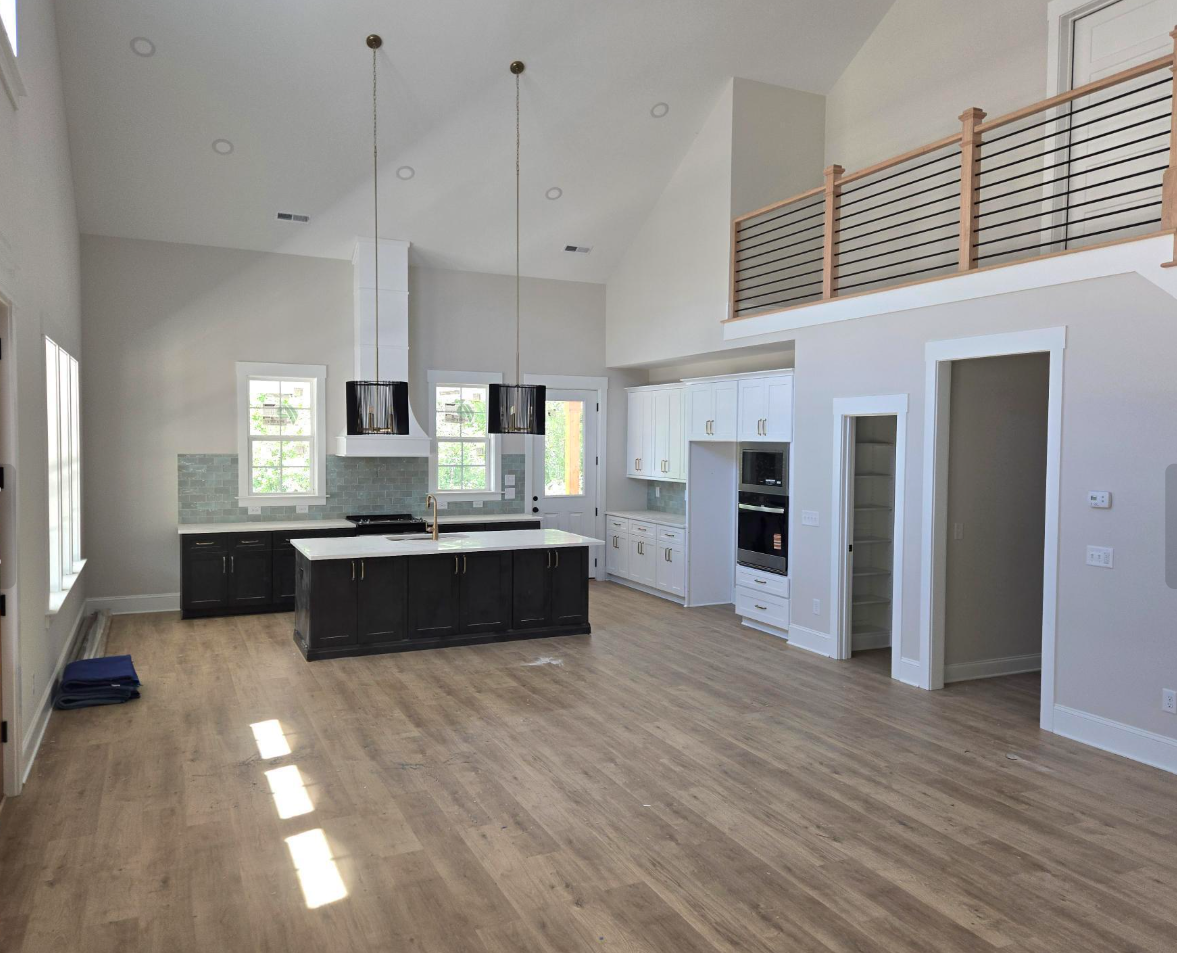 Bright modern open-plan kitchen and living space with wood floors, white walls, an island, and a loft railing.