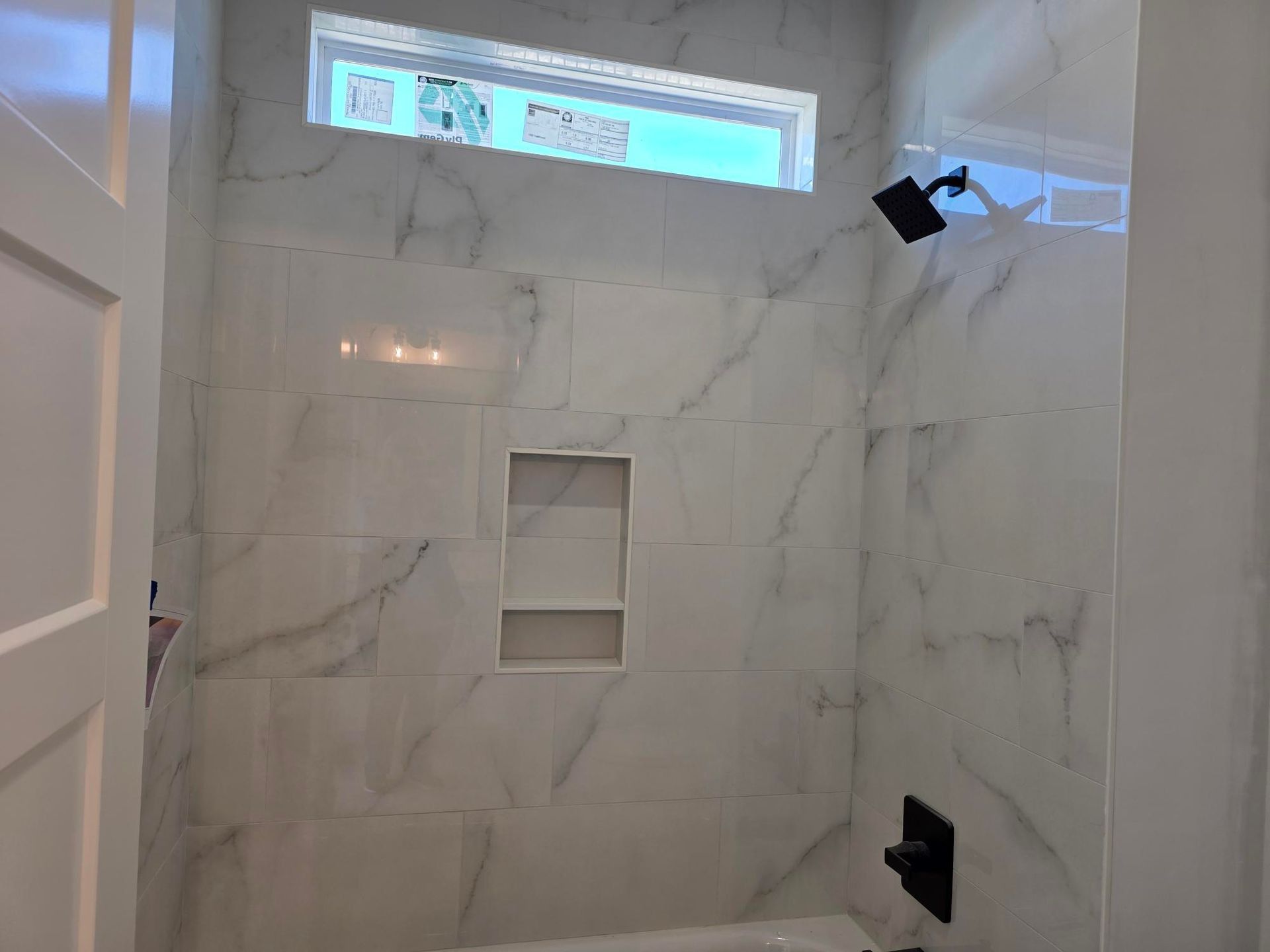 White marble-tile shower with built-in niche, small window, and black shower fixtures