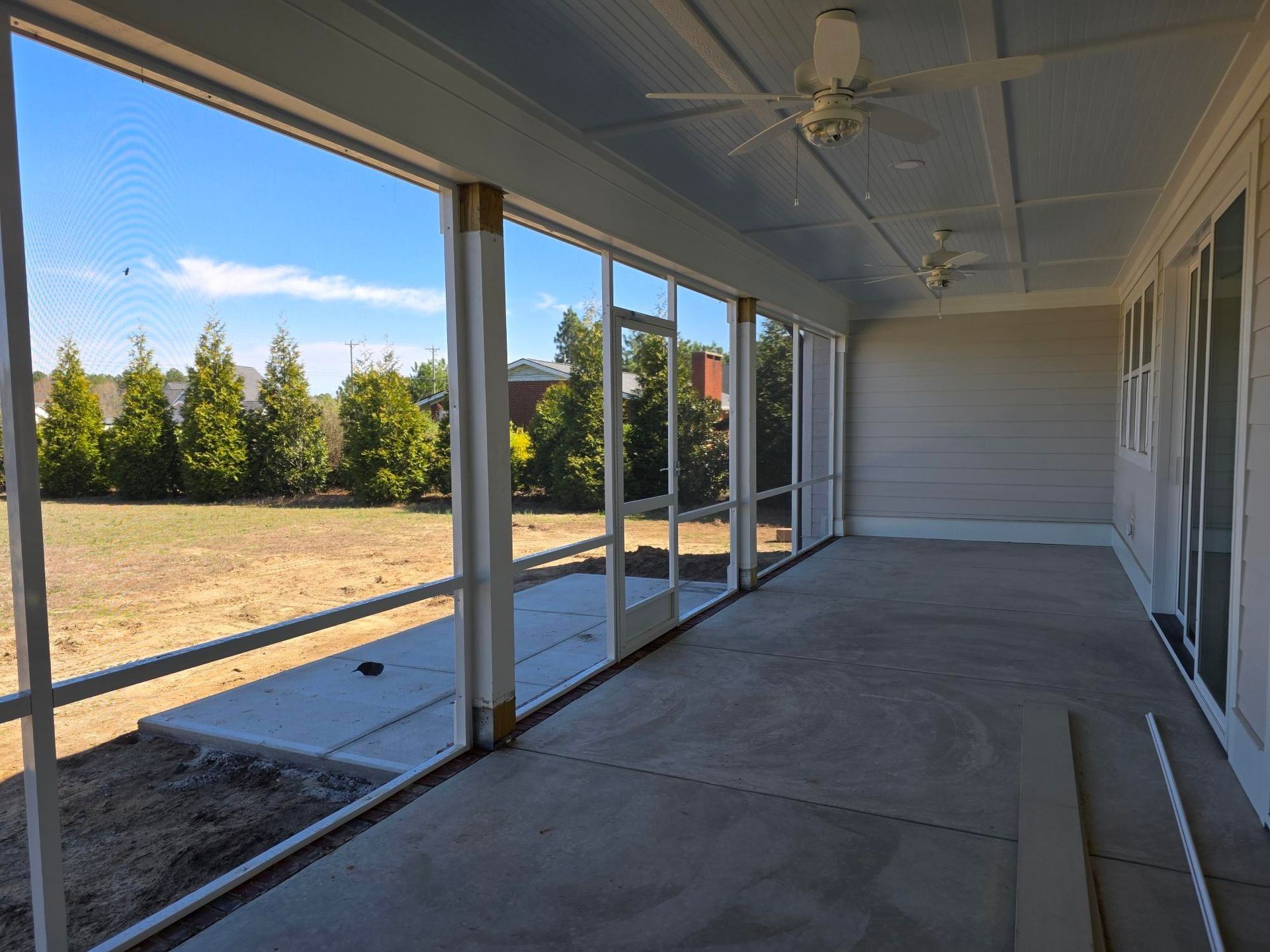 Covered patio with concrete floor, sliding glass doors, and a view of a grassy yard and trees
