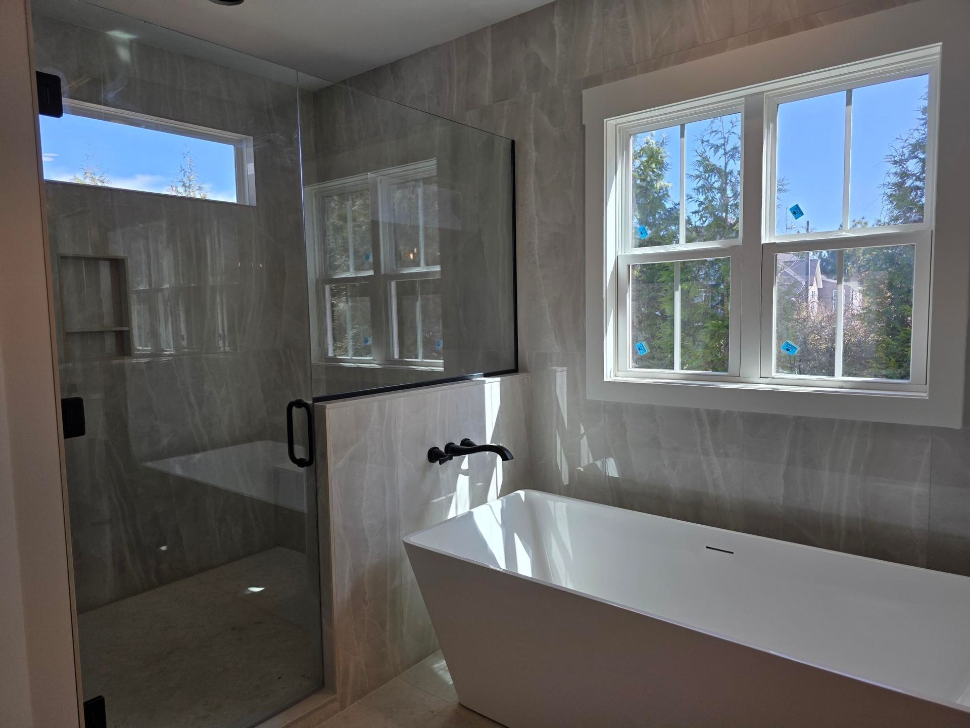 Modern bathroom with freestanding white tub, glass shower, and two windows letting in daylight
