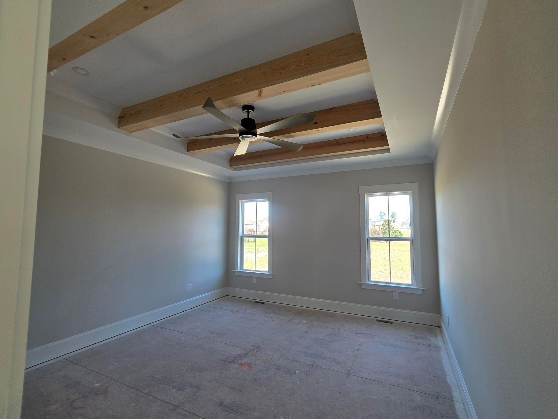Empty unfinished room with exposed ceiling beams, gray walls, and two windows.