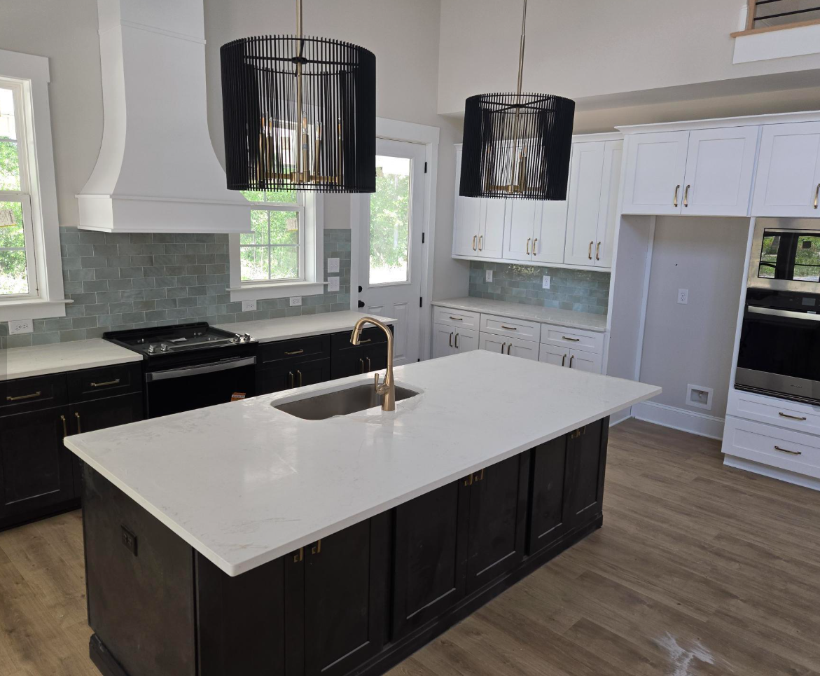 Modern white kitchen with black island, pendant lights, stainless fridge, and large windows