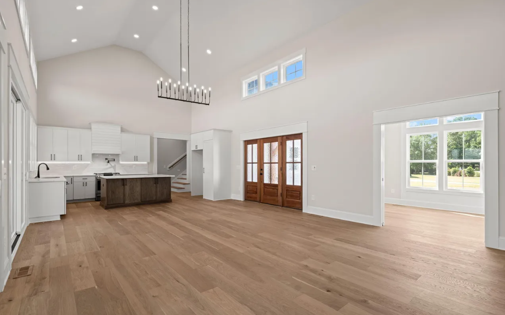 Bright open living room with kitchen, wood floors, high ceilings, and large windows.