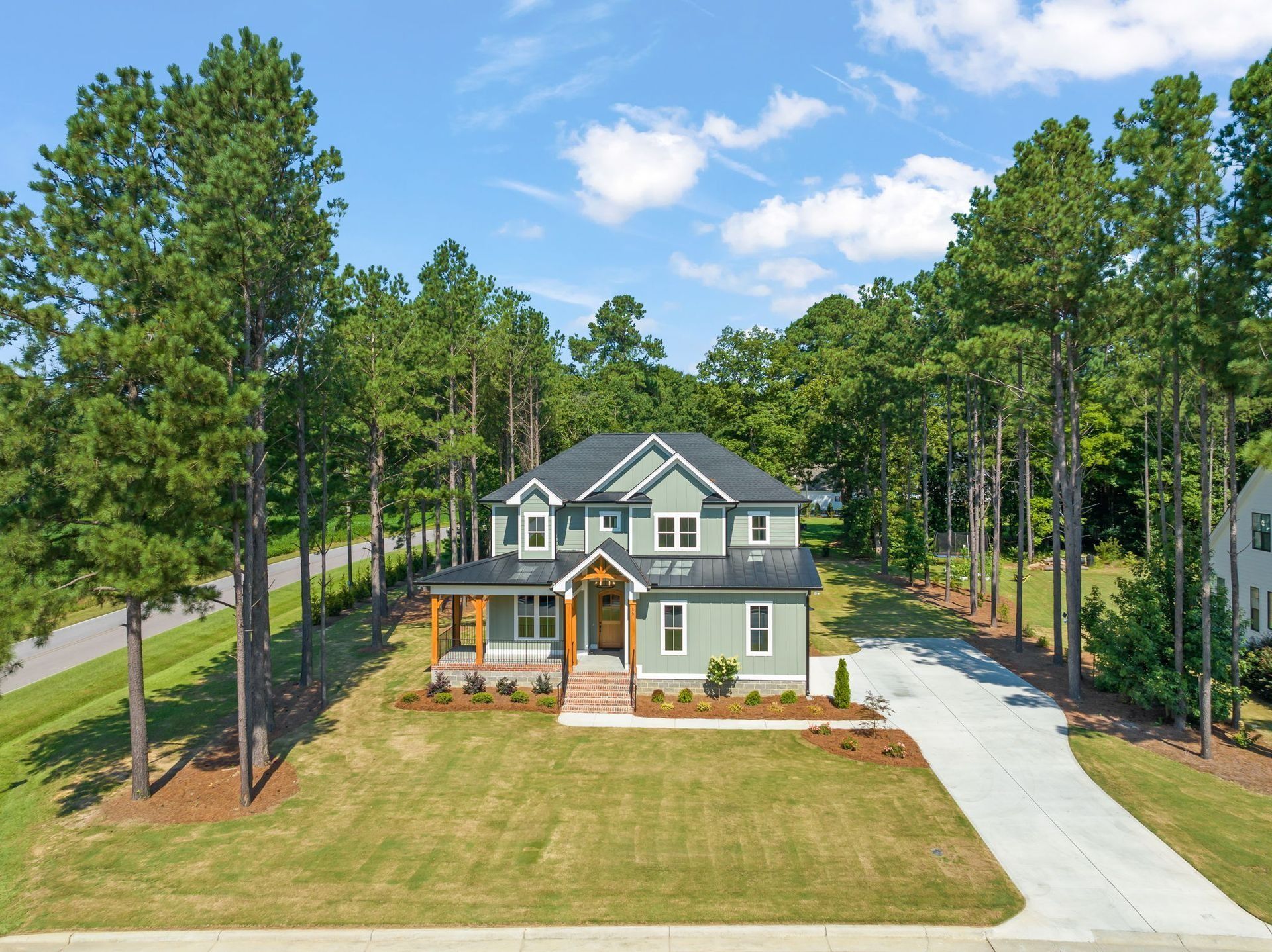 Aerial view of a large white house with green roof, front porch, driveway, and trees on a sunny day