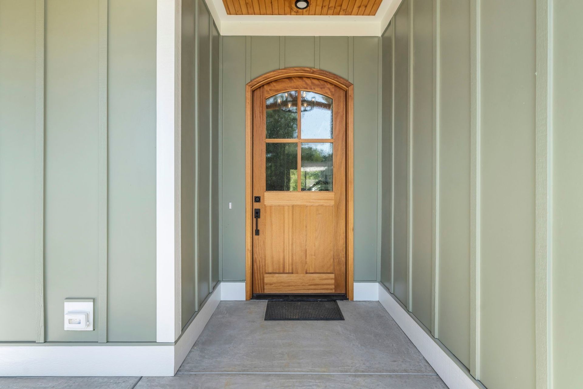 Front porch with a wooden front door, green siding, and a gray entry mat
