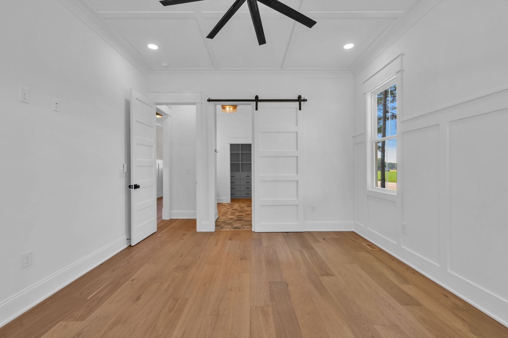 Bright empty room with white walls, hardwood floors, ceiling fan, and sliding barn door.