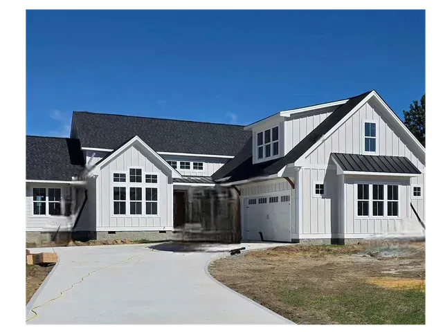 Large white suburban house with black roof, front driveway, and garage under a clear blue sky