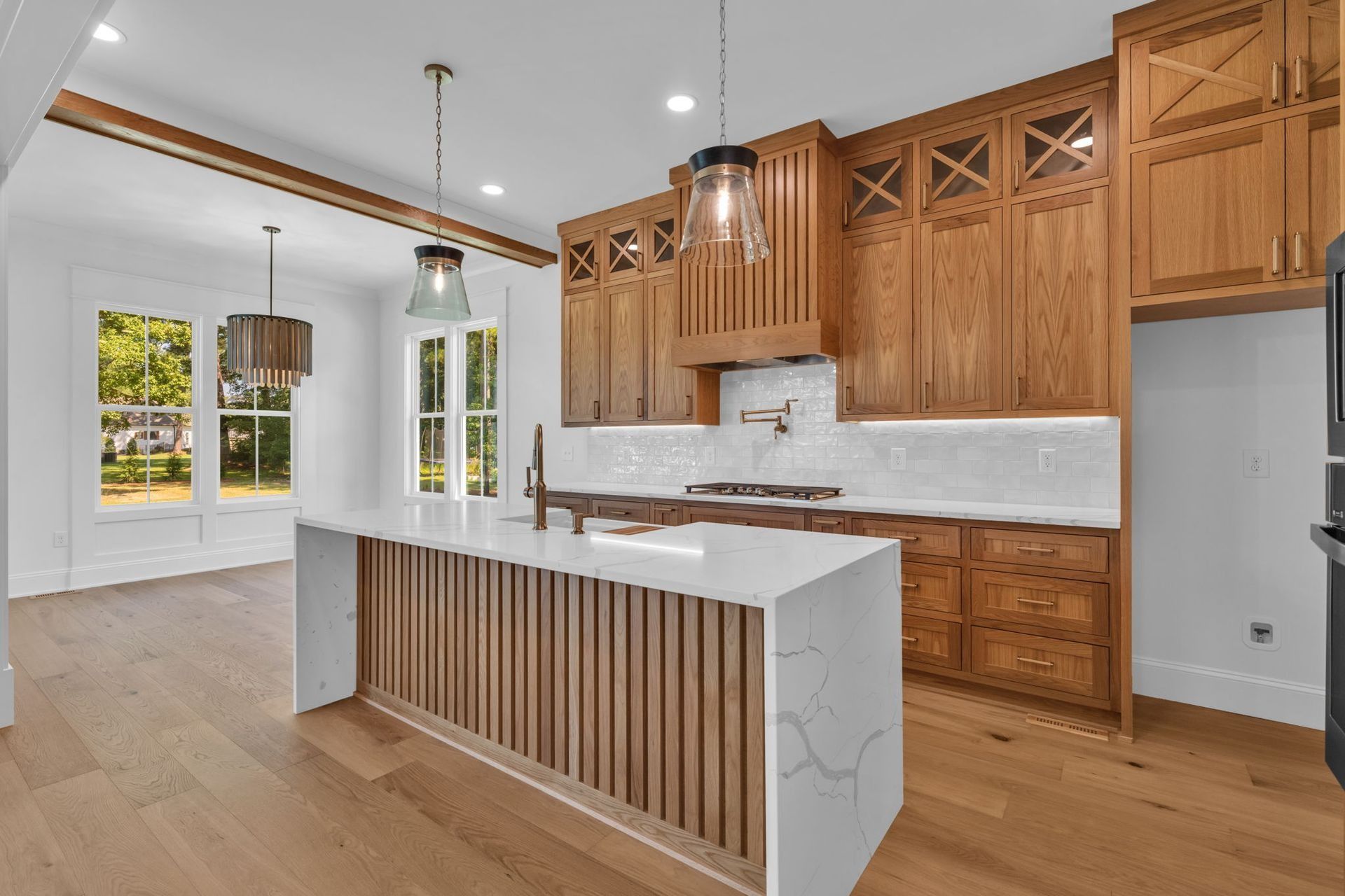 Modern kitchen with wood cabinets, white island, pendant lights, and hardwood floors