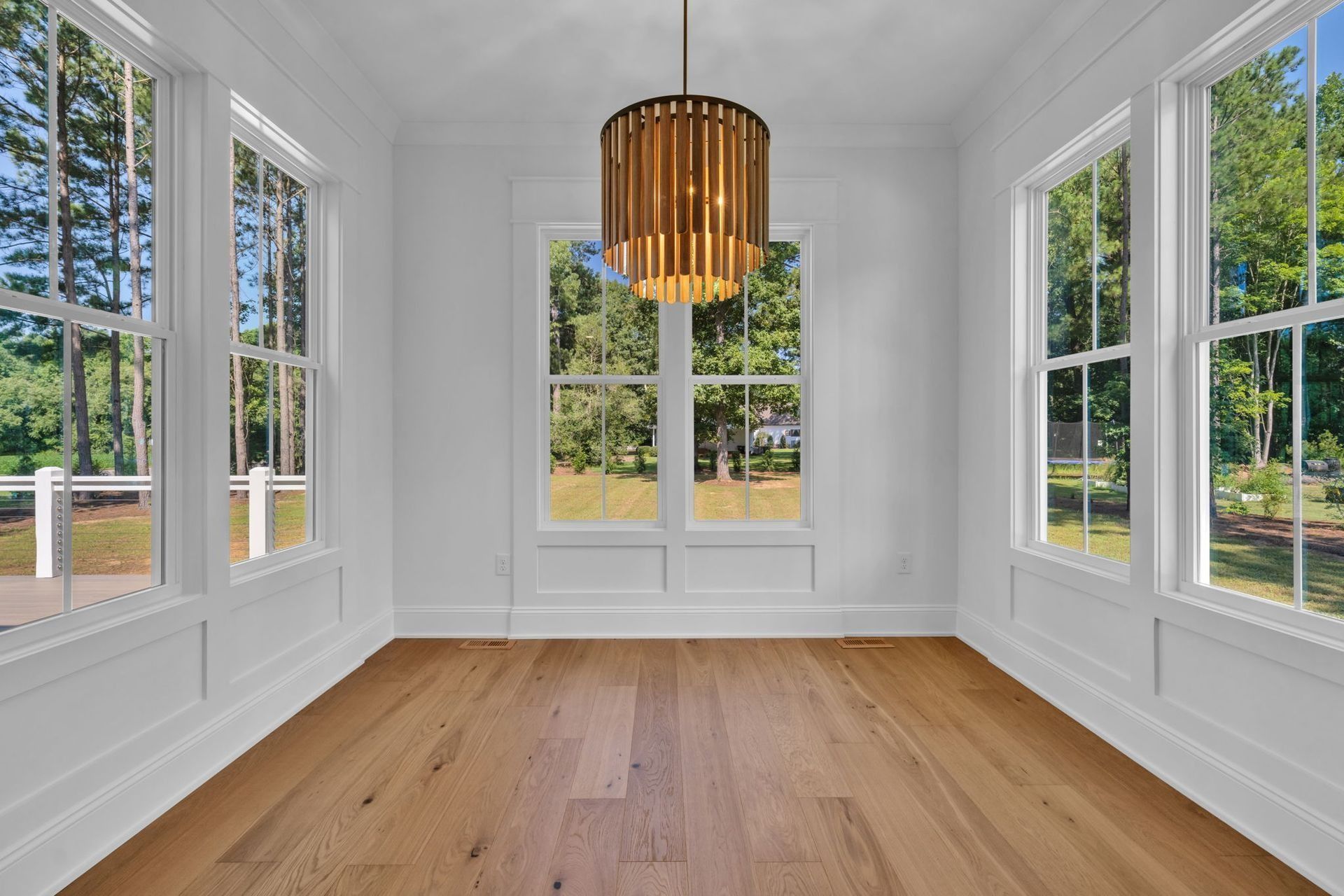 Bright empty sunroom with hardwood floor, white walls, large windows, and a modern pendant light