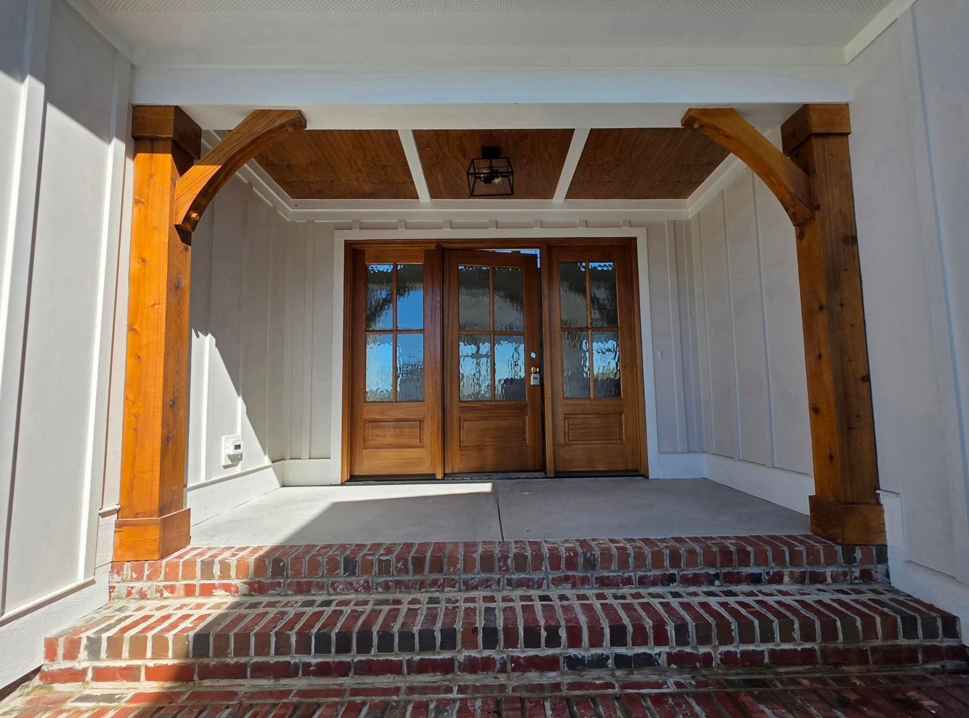 Covered brick porch with wooden columns and double front doors underneath a white ceiling