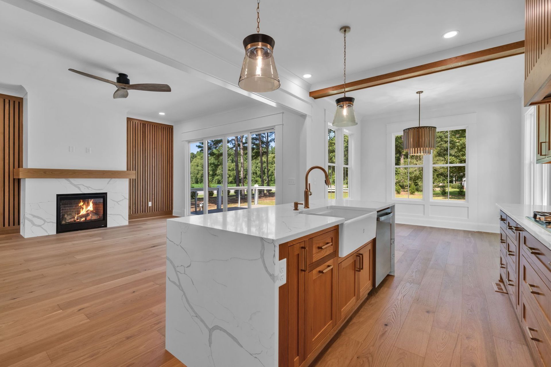 Bright modern kitchen and living room with white walls, wood floors, island, fireplace, and large windows