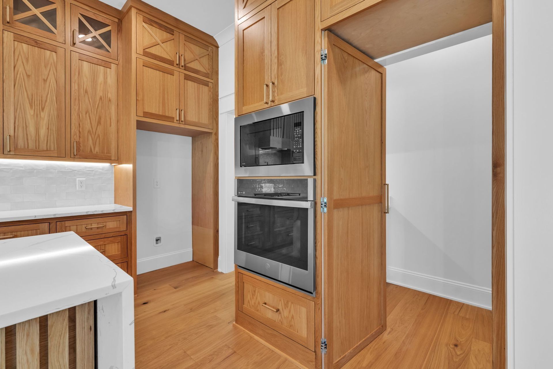 Warm wood kitchen with built-in double ovens and white tile backsplash.