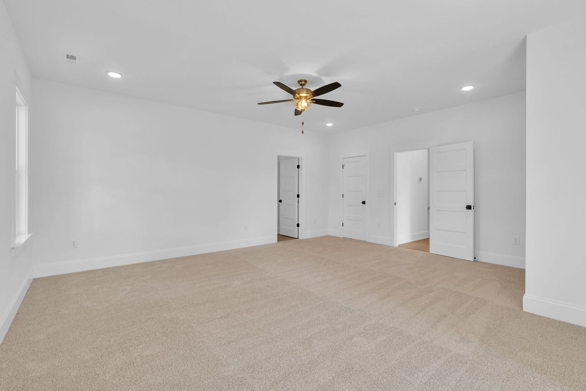 Empty carpeted bedroom with white walls, ceiling fan, recessed lights, and two open doors