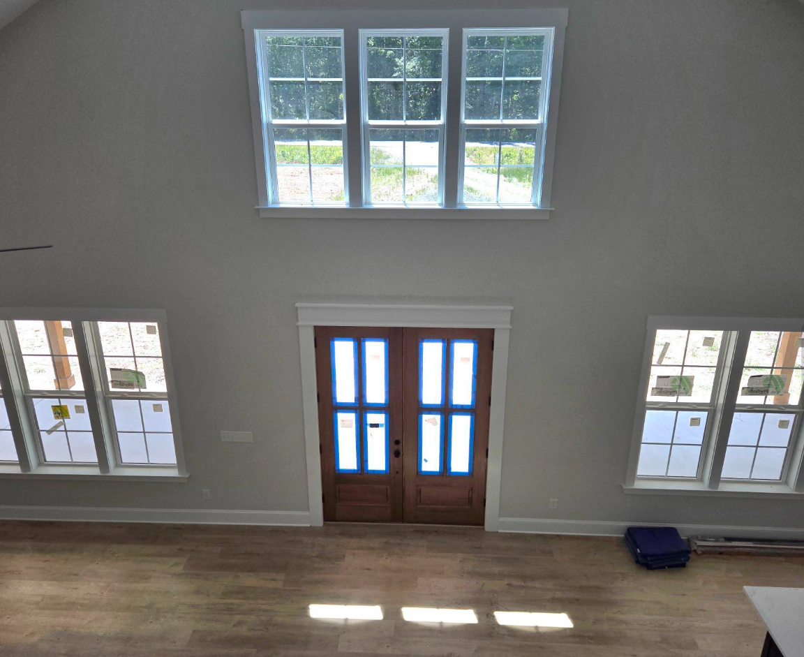 Bright foyer with wooden front doors, tall windows, and sunlight on hardwood floors.