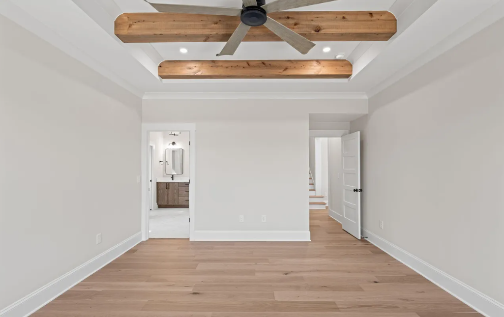 Empty modern bedroom with wood floors, white walls, and a ceiling fan