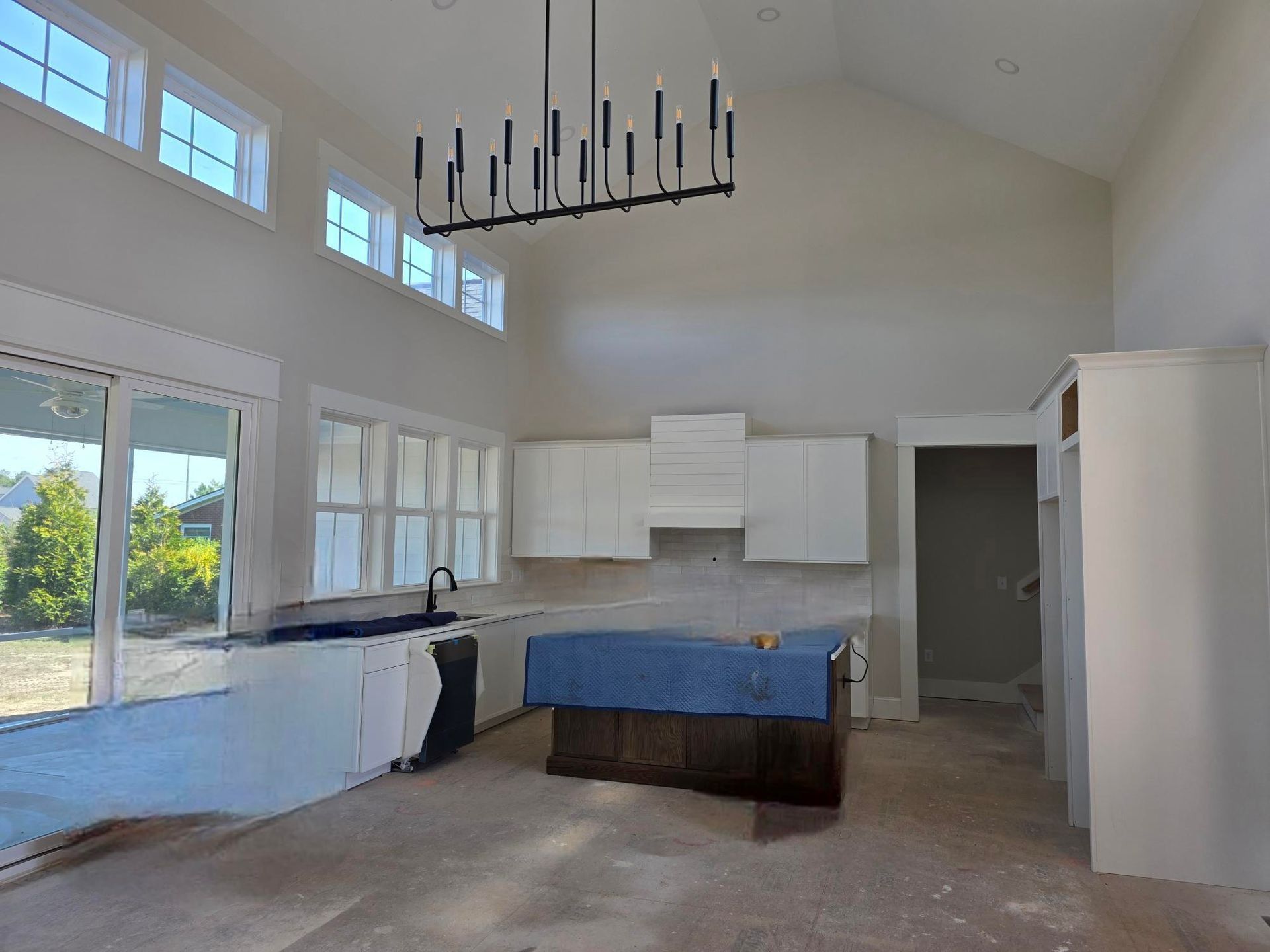 Empty bright kitchen with high ceiling, white cabinets, blue island, and sliding glass doors.