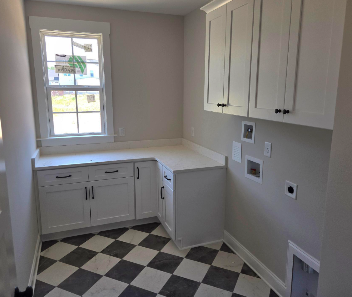Small kitchen with white cabinets, gray walls, black-and-white checkered floor, and a window over the sink.