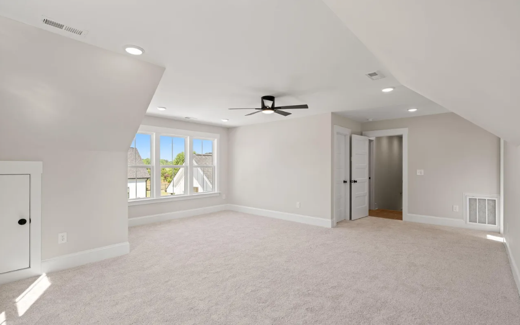 Bright empty living room with vaulted ceiling, ceiling fan, carpet, and large windows.
