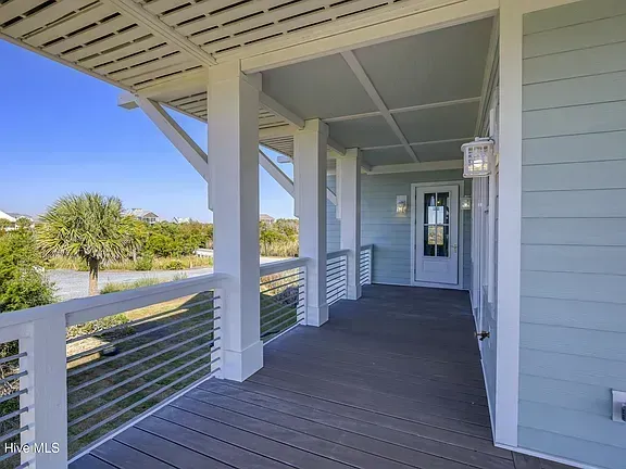 Covered front porch with gray siding, wooden floor, white railings, and a hanging lantern overlooking a yard.