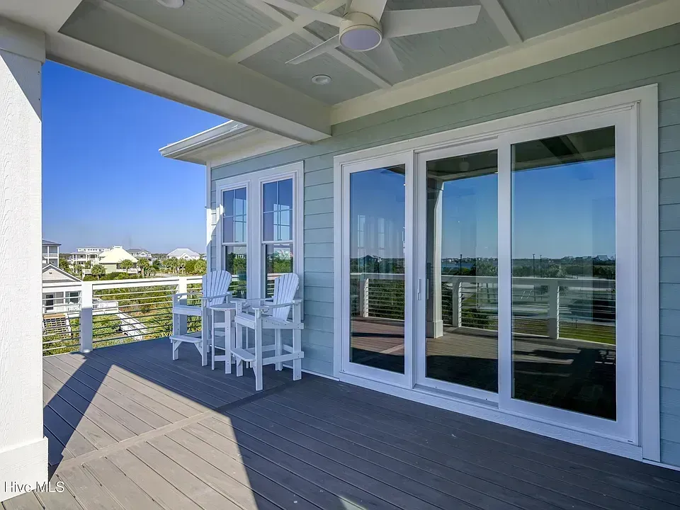 Covered balcony with white chairs, sliding glass doors, and ocean view on a sunny day