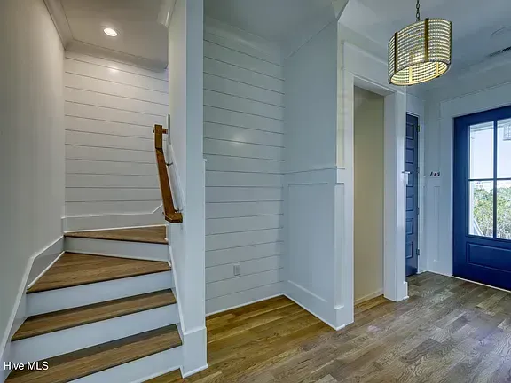 Bright hallway with white shiplap walls, wood floors, stairs, and a blue front door.