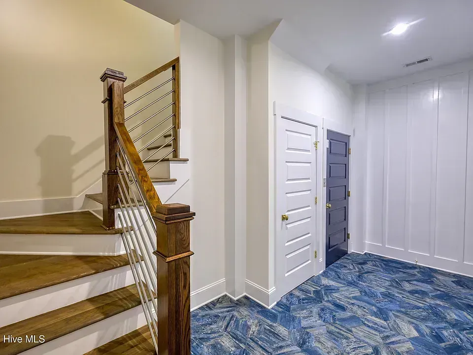 Interior entryway with blue patterned carpet, white closet doors, and a wooden staircase railing
