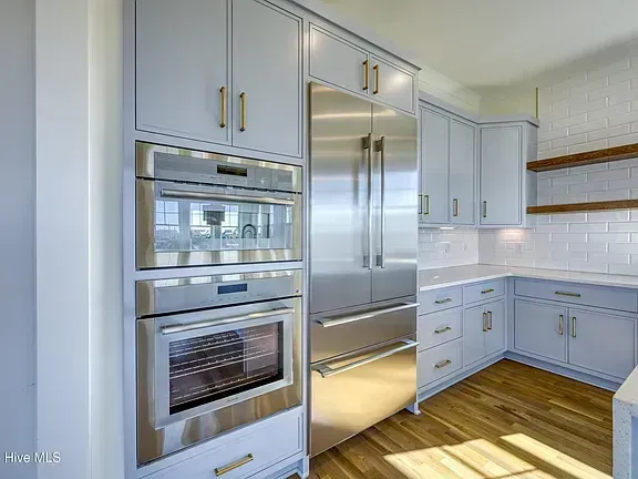 Bright white kitchen with stainless steel double oven, French-door refrigerator, and wood floors.