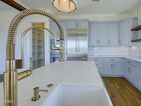 Modern white kitchen with large island, brass faucet, and stainless steel refrigerator