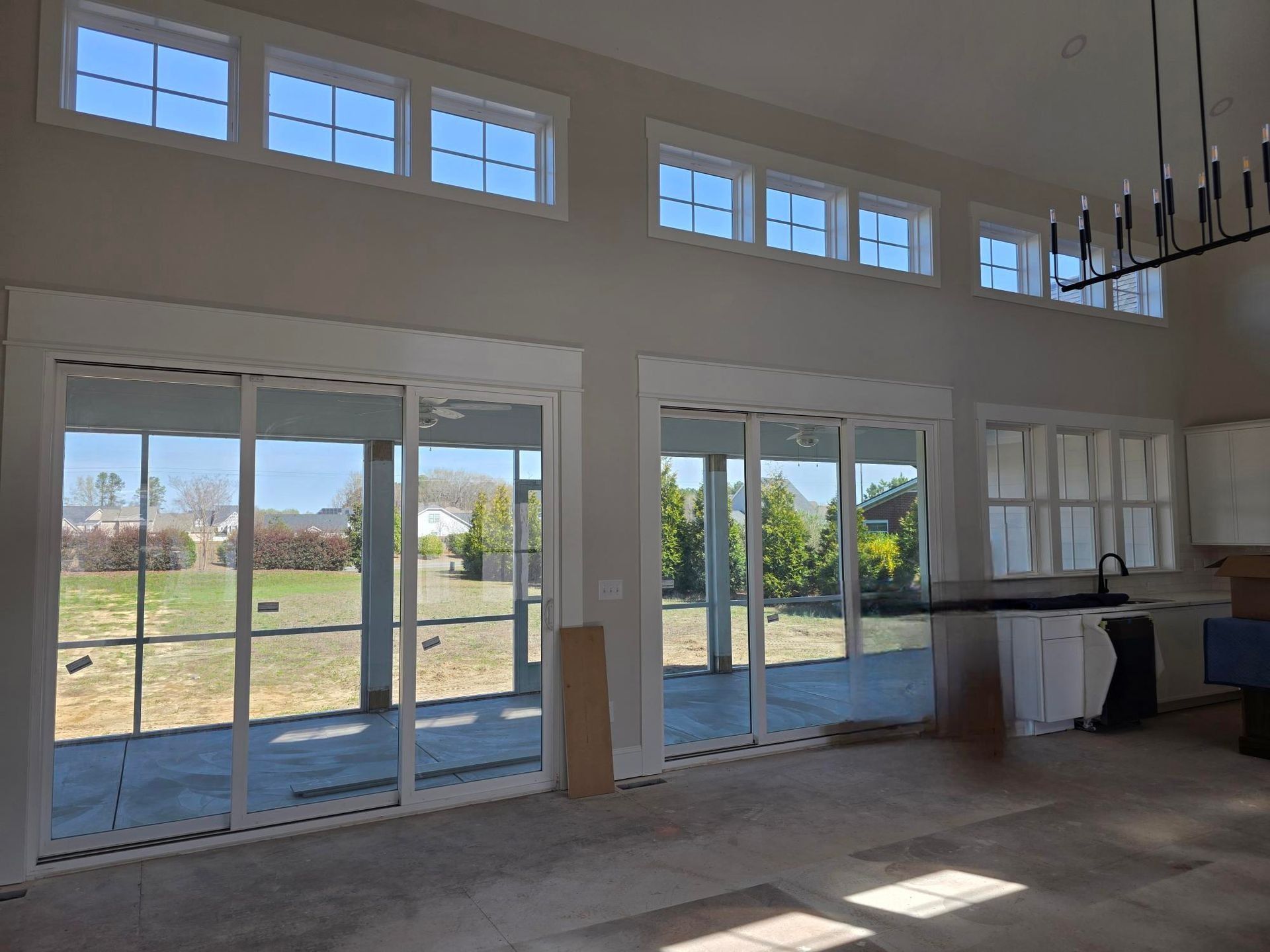 Bright open room with large glass doors and windows overlooking a grassy yard; sunlight on the floor.