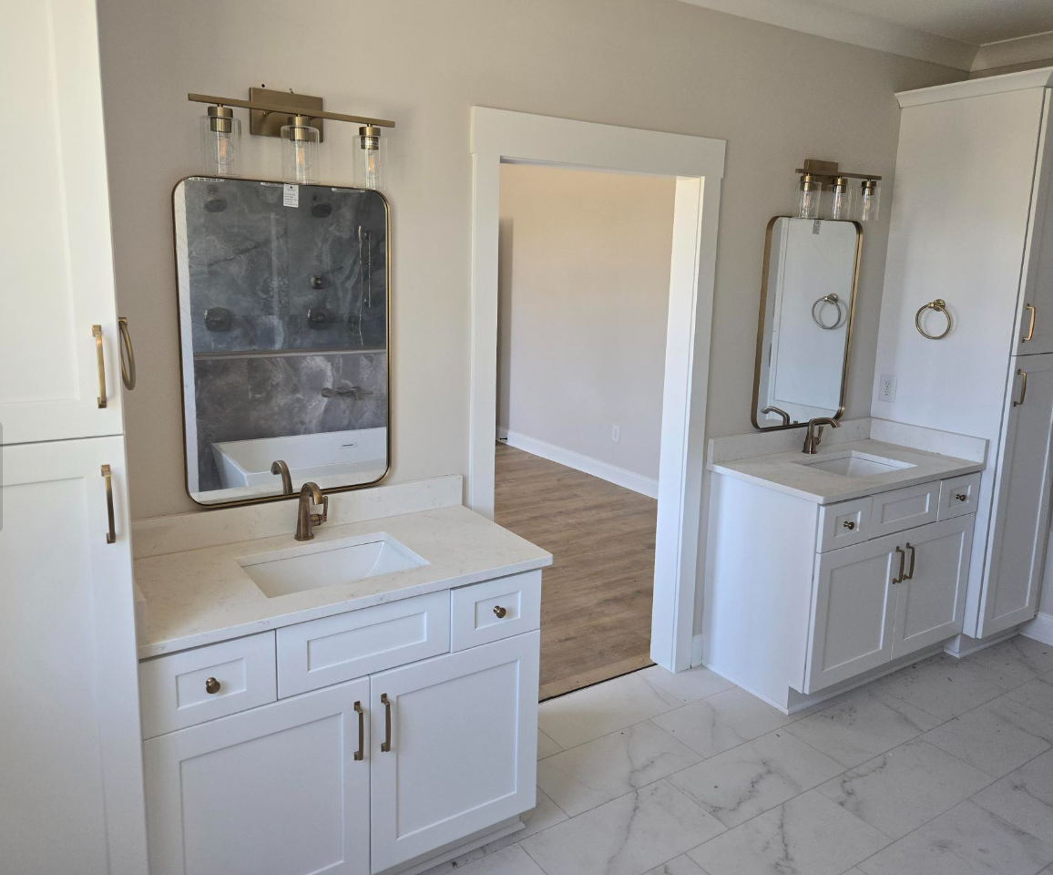 Bright white bathroom vanity with mirrors and doorway to adjoining room, marble-look floor.